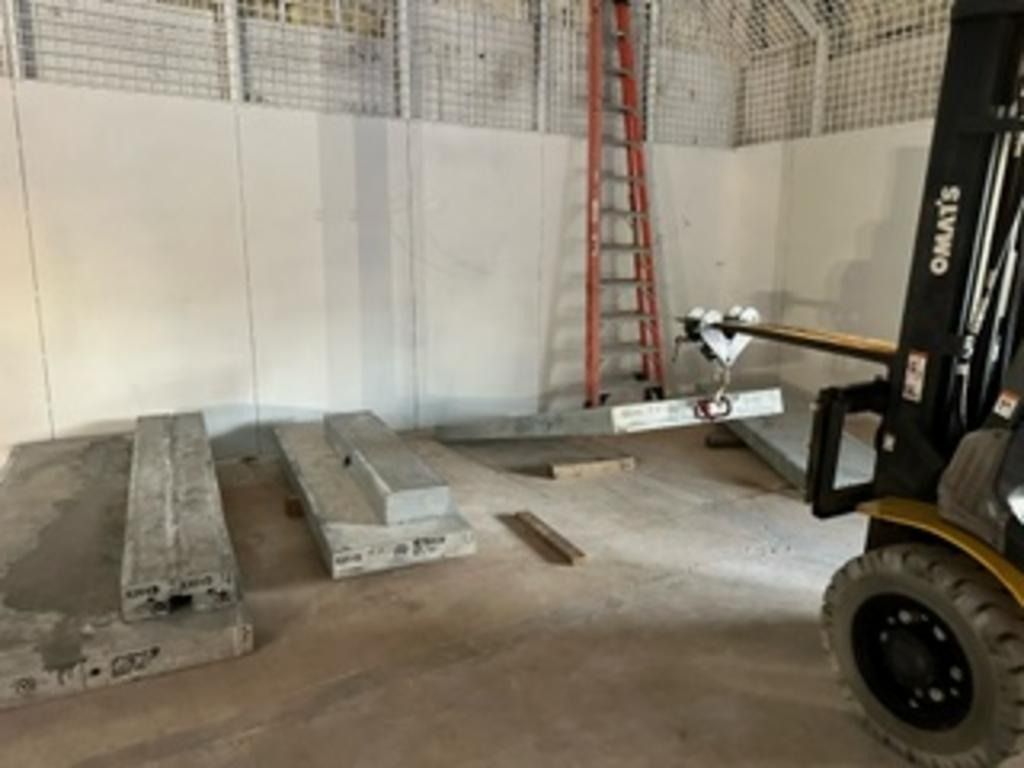 Forklift in warehouse lifting concrete slabs beside stacked slabs and a red ladder.