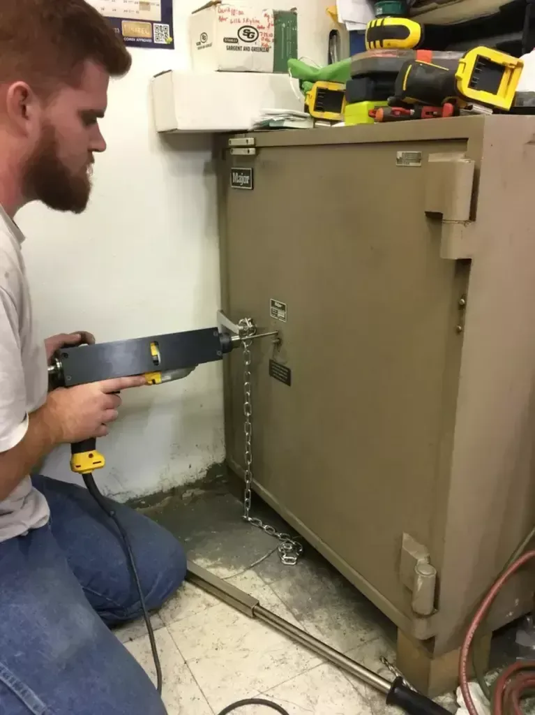 Person using a tool to cut into the side of a large beige appliance in a workshop.