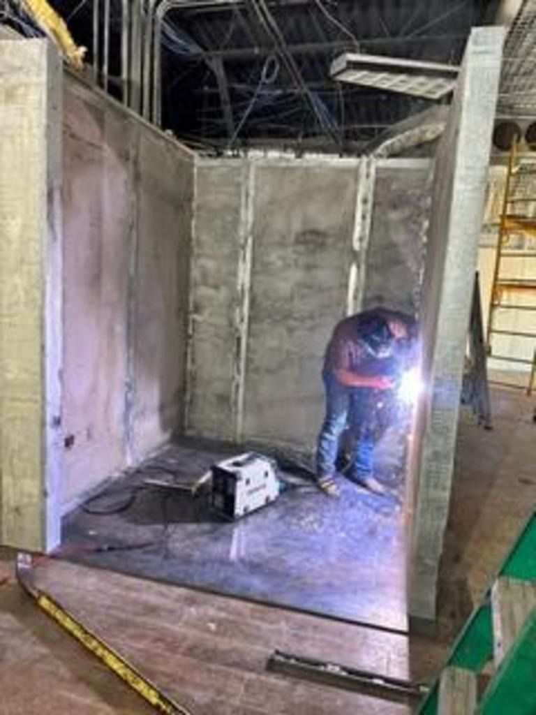 Person welding inside a half-built room with concrete walls and construction tools on the floor