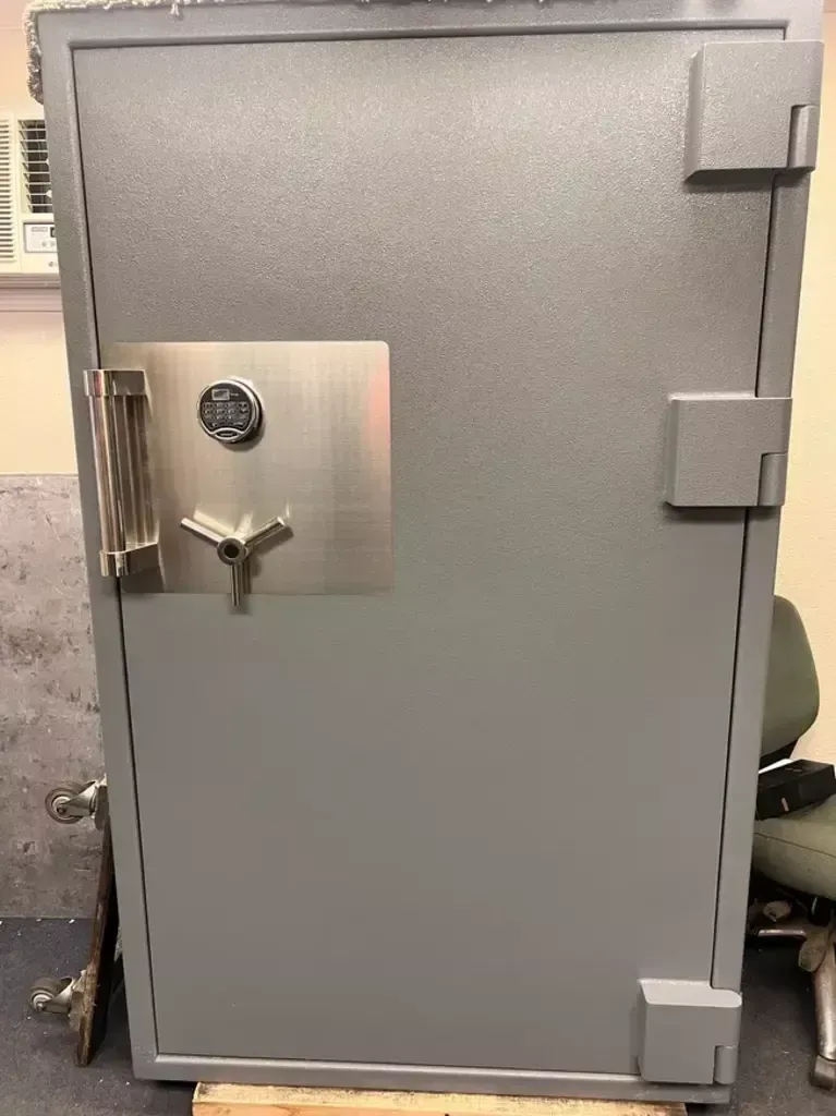 Gray secure vault door with heavy hinges and a combination lock on a stainless-steel panel