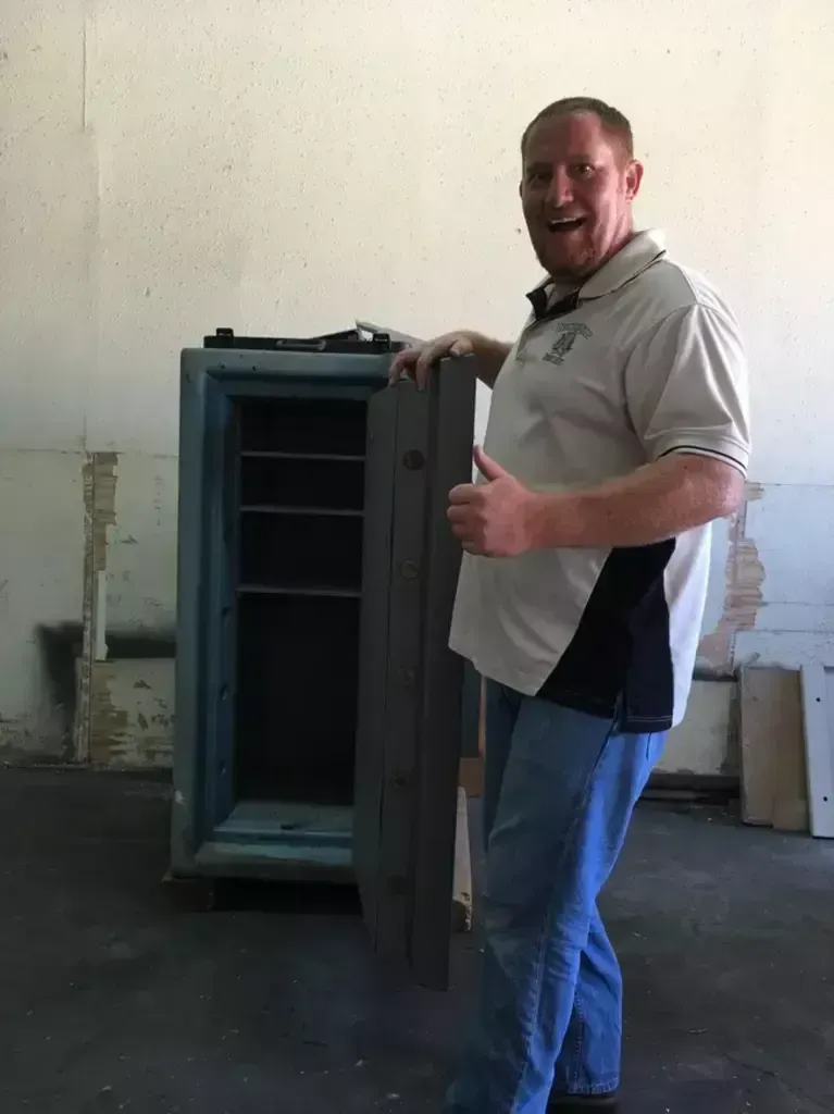 Man opening a gray metal cabinet in a bare room, smiling at the camera.