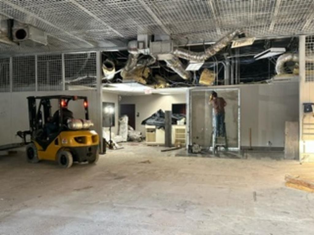 Interior construction site with forklift, exposed ceiling, and worker near a framed wall opening
