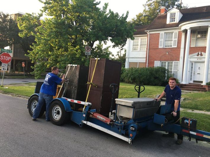 Two people loading furniture onto a blue trailer on a residential street.