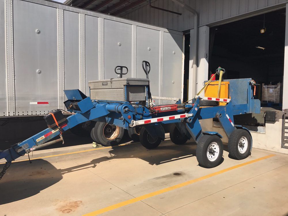Blue agricultural trailer with large wheels parked outside a warehouse loading bay