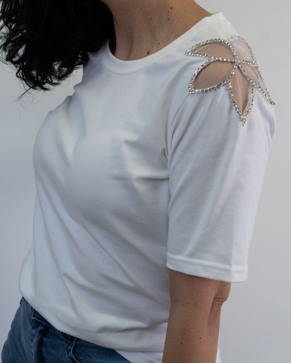 Mujer que lleva una camiseta blanca con un diseño floral brillante en los hombros, toma en ángulo.