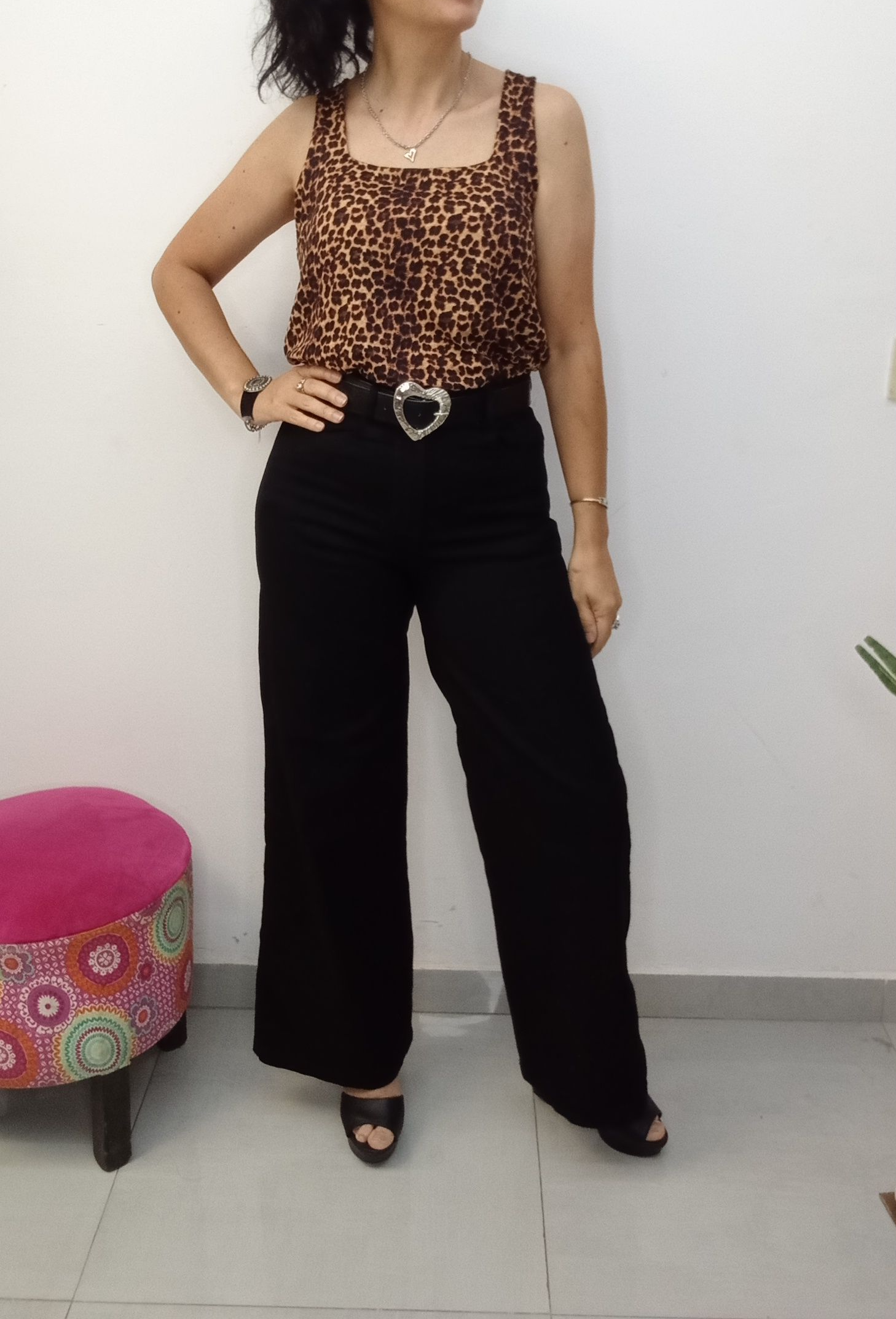 Mujer con top rosa y vaqueros anchos, con las manos en las caderas. Sandalias de plataforma beige, pared blanca.