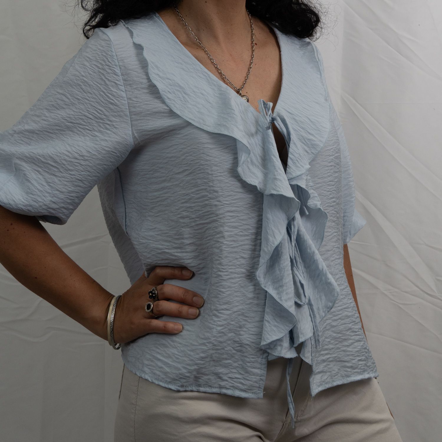 Mujer con blusa azul con volantes y mangas cortas, posando con la mano en la cadera.