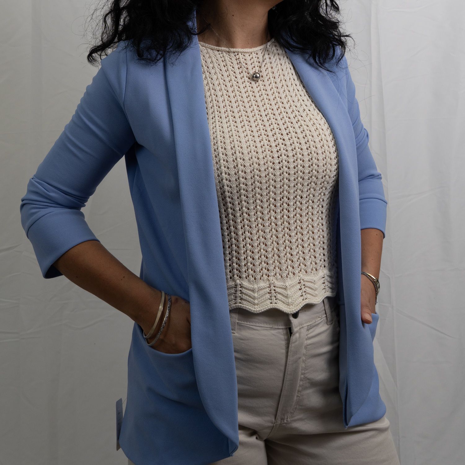 Mujer con blazer azul, top color crema, manos en los bolsillos, posando en el interior.