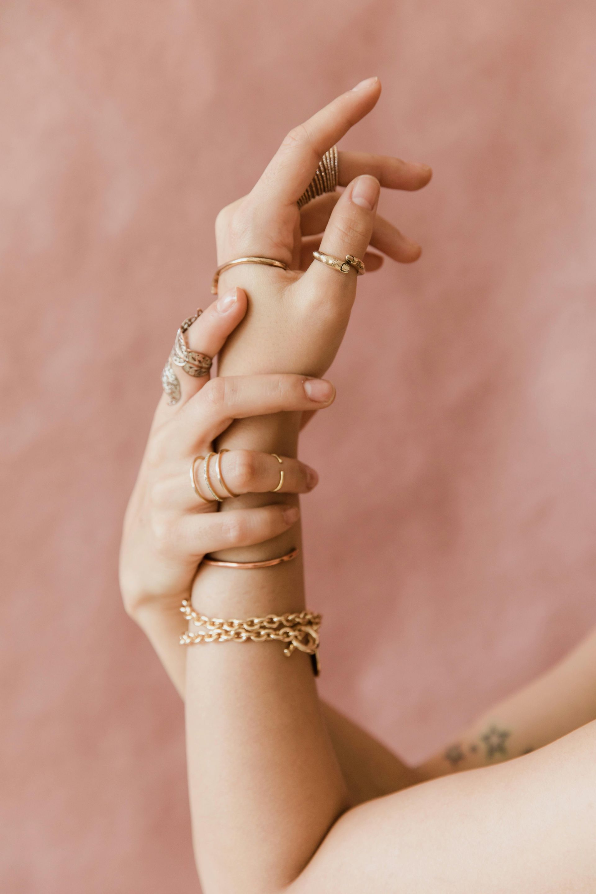 Manos con joyas de oro, sobre un fondo rosa.