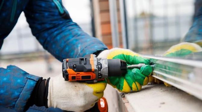Hands in gloves using an orange power drill on a metal railing outdoors