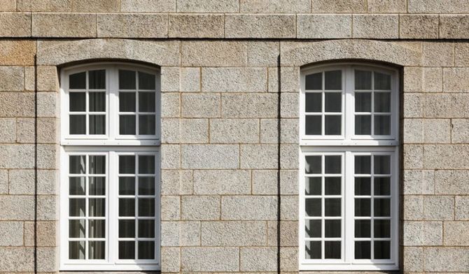 Two white-framed windows set in a tan stone wall
