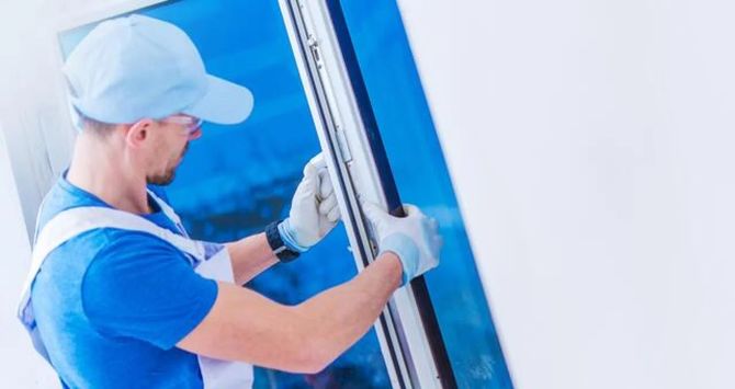 Worker in blue cap and shirt installing a window frame inside a bright room