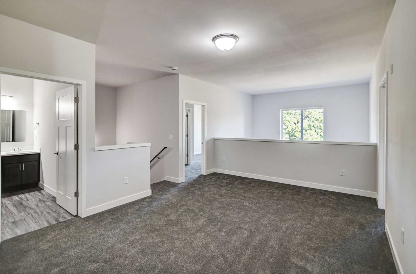 An empty room with a carpeted floor and a staircase leading to the second floor.
