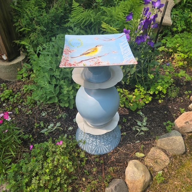 Blue handmade bird bath beside garden flowers