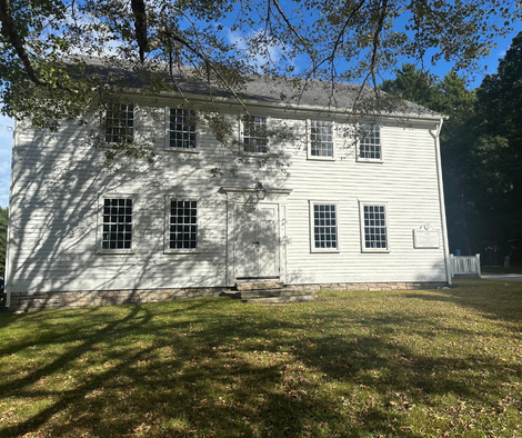 White two-story house with many windows and a small deck, under trees in a grassy yard