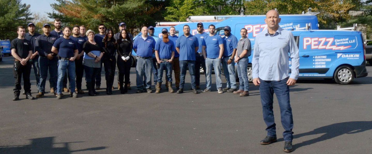 Group of people standing in a parking lot beside a blue PEZZ truck and van with branding.