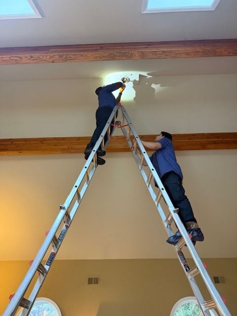 Two workers on ladders repairing a ceiling light in a room