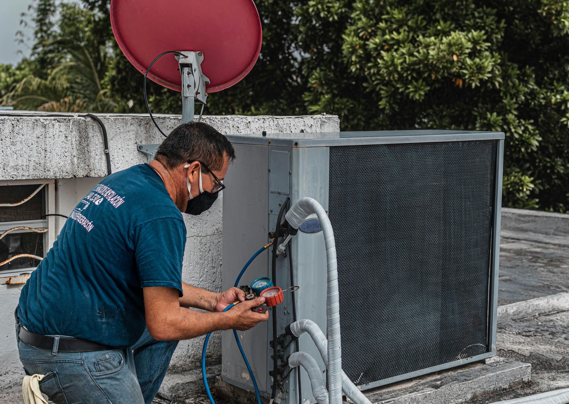 Technician working on rooftop HVAC unit beside a red satellite dish