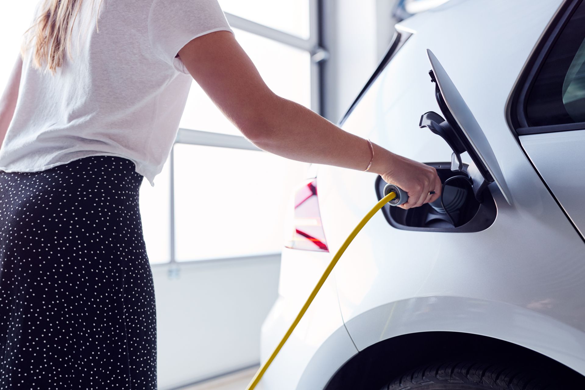 Person charging a silver electric car with a yellow cable in a garage