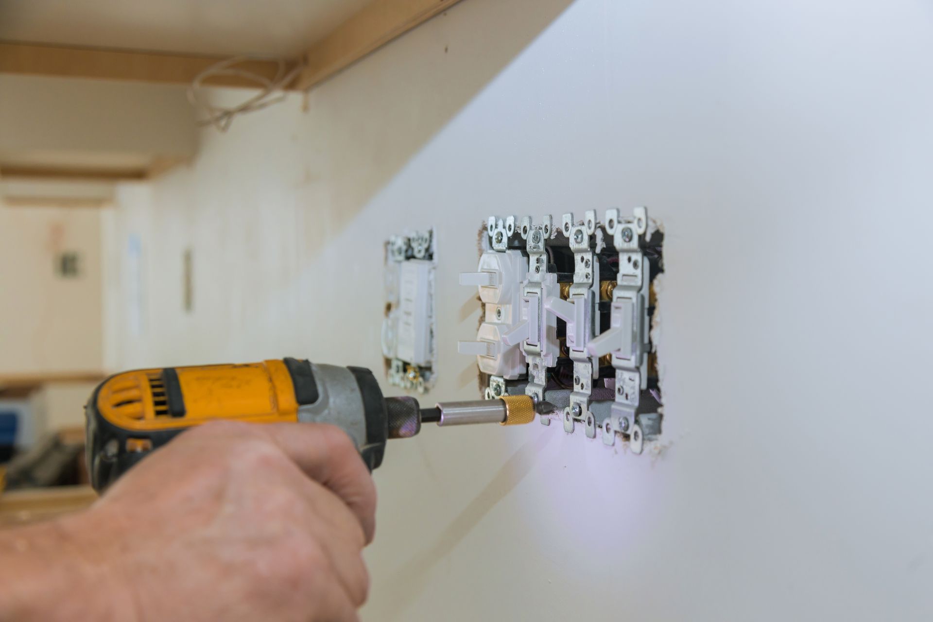 Hand drilling through a white wall to install an electrical outlet box