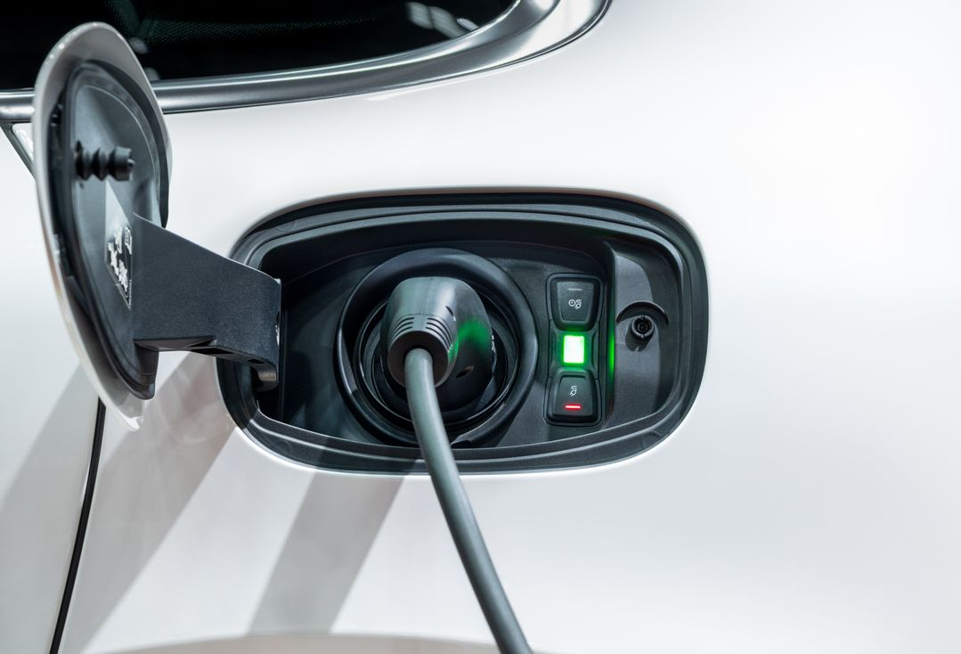 Electric car charging port with plug connected and green indicator lights on a white vehicle