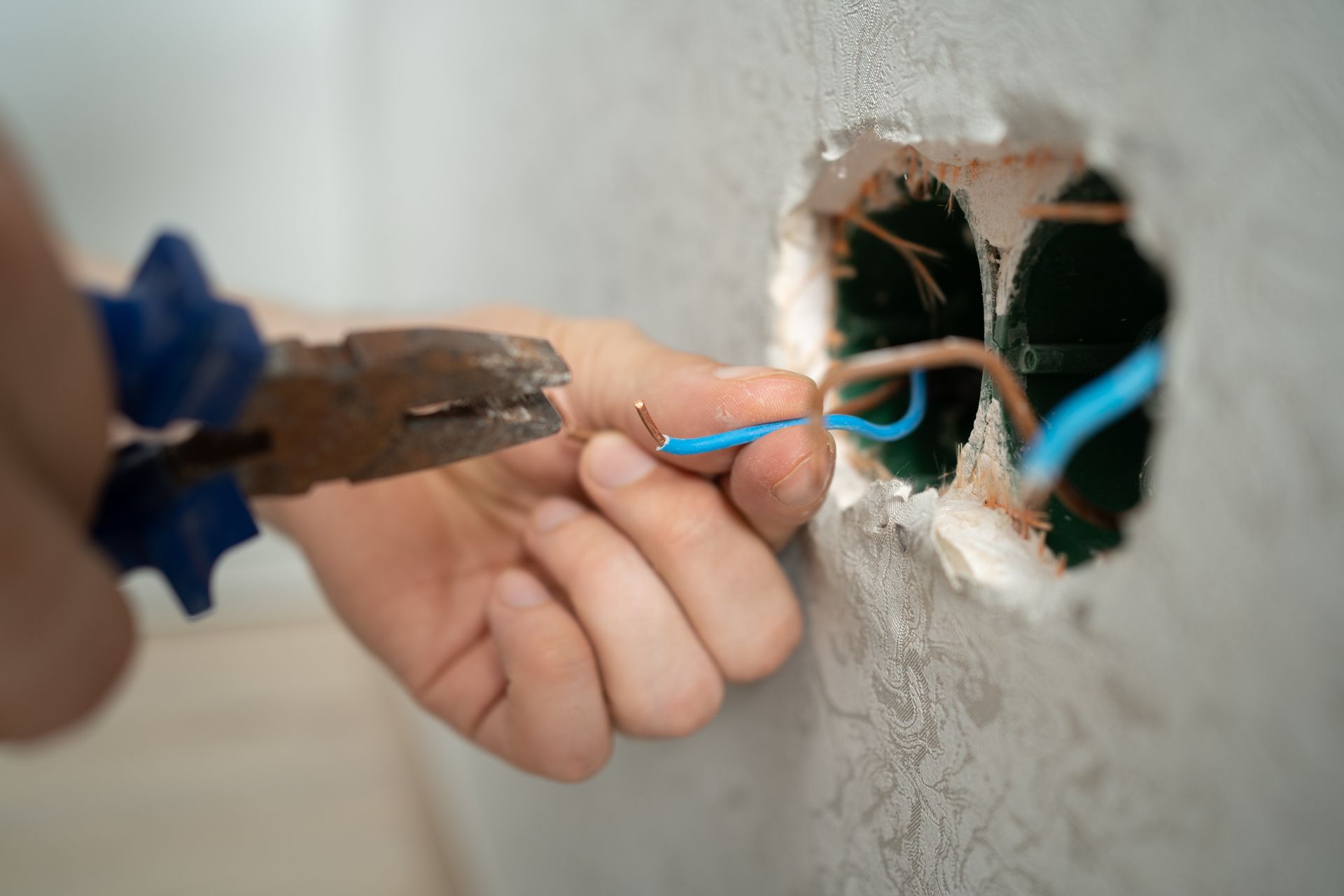 Hands using pliers to connect blue wires through a hole in a wall