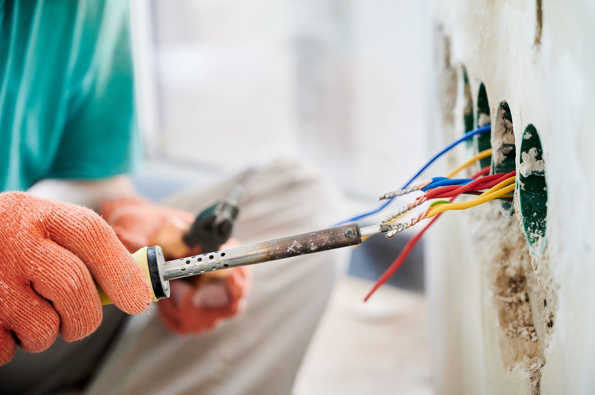 Gloved electrician wiring exposed cables into a wall outlet box