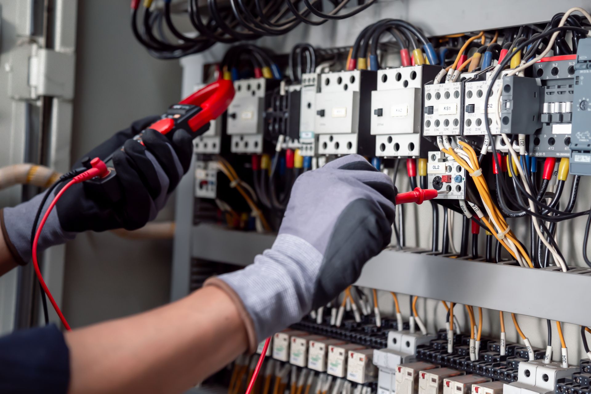 Technician testing electrical control panel wiring with insulated tools and gloves