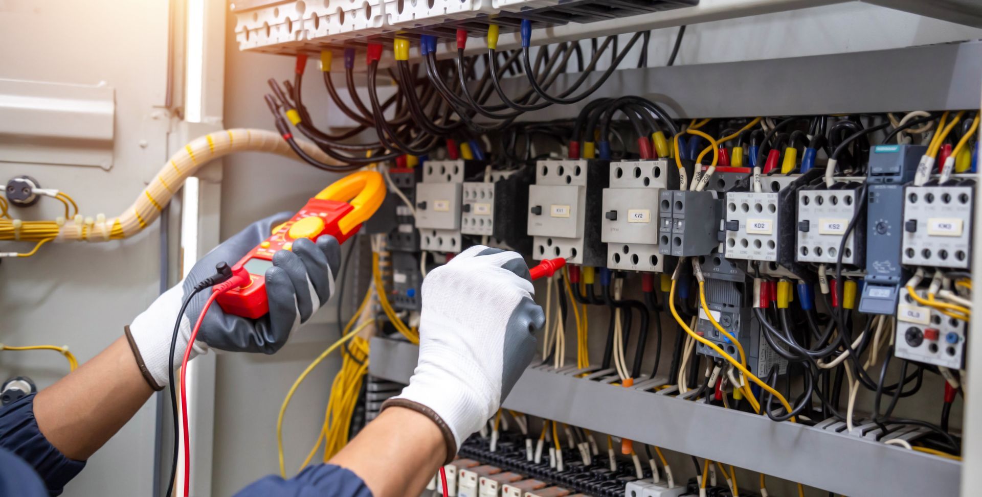 Technician in gloves tests wiring inside an electrical control panel with a multimeter and probes