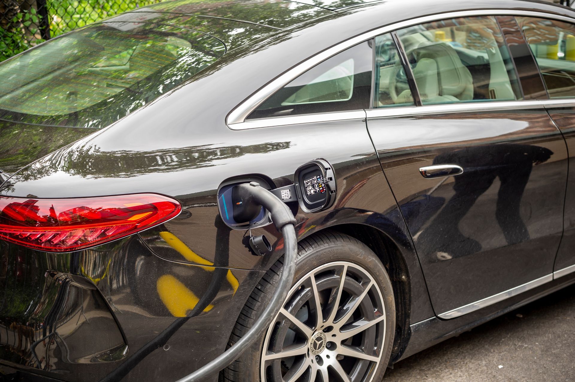 Black sedan charging at an EV station outdoors, with a cable plugged into the rear side.
