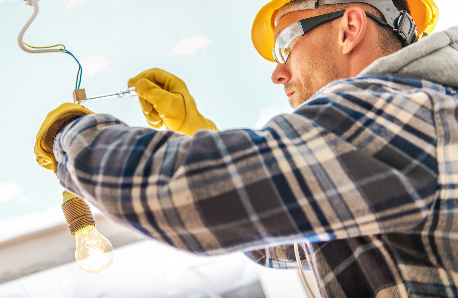Electrician in hard hat and safety glasses wiring a ceiling light fixture