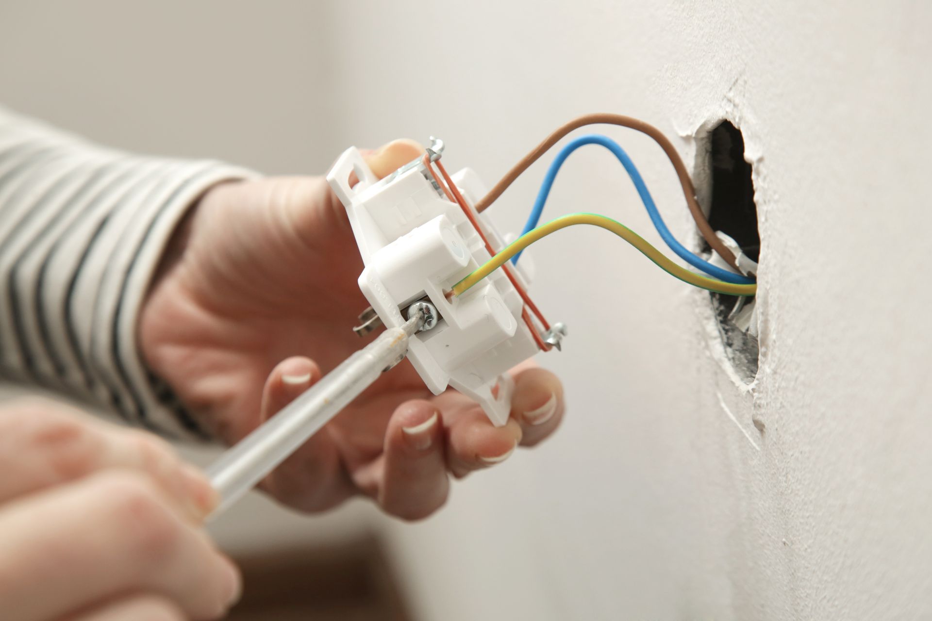 Hands wiring an electrical outlet into a wall opening with a screwdriver