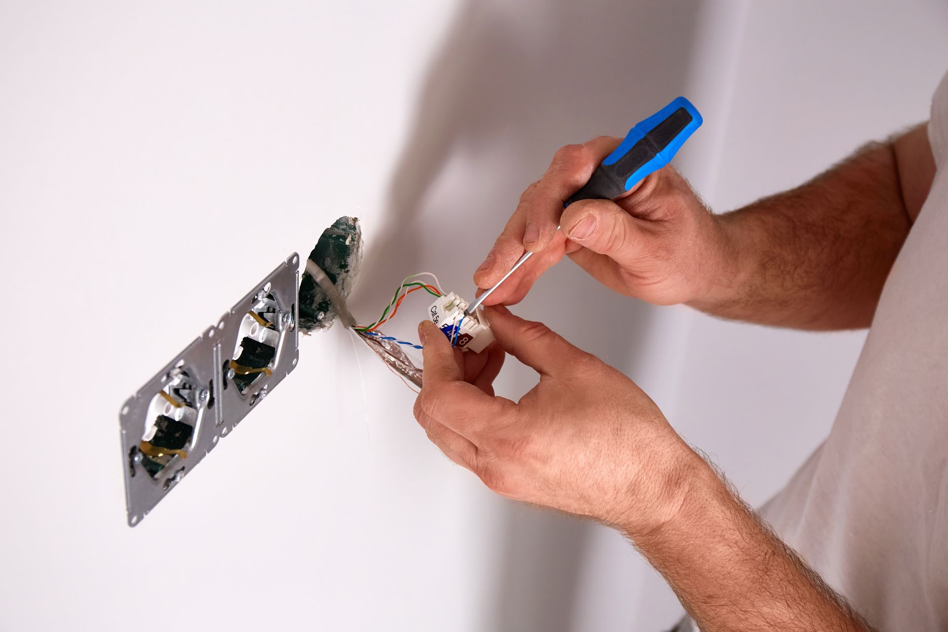Hands using a screwdriver to wire an electrical outlet in a wall.