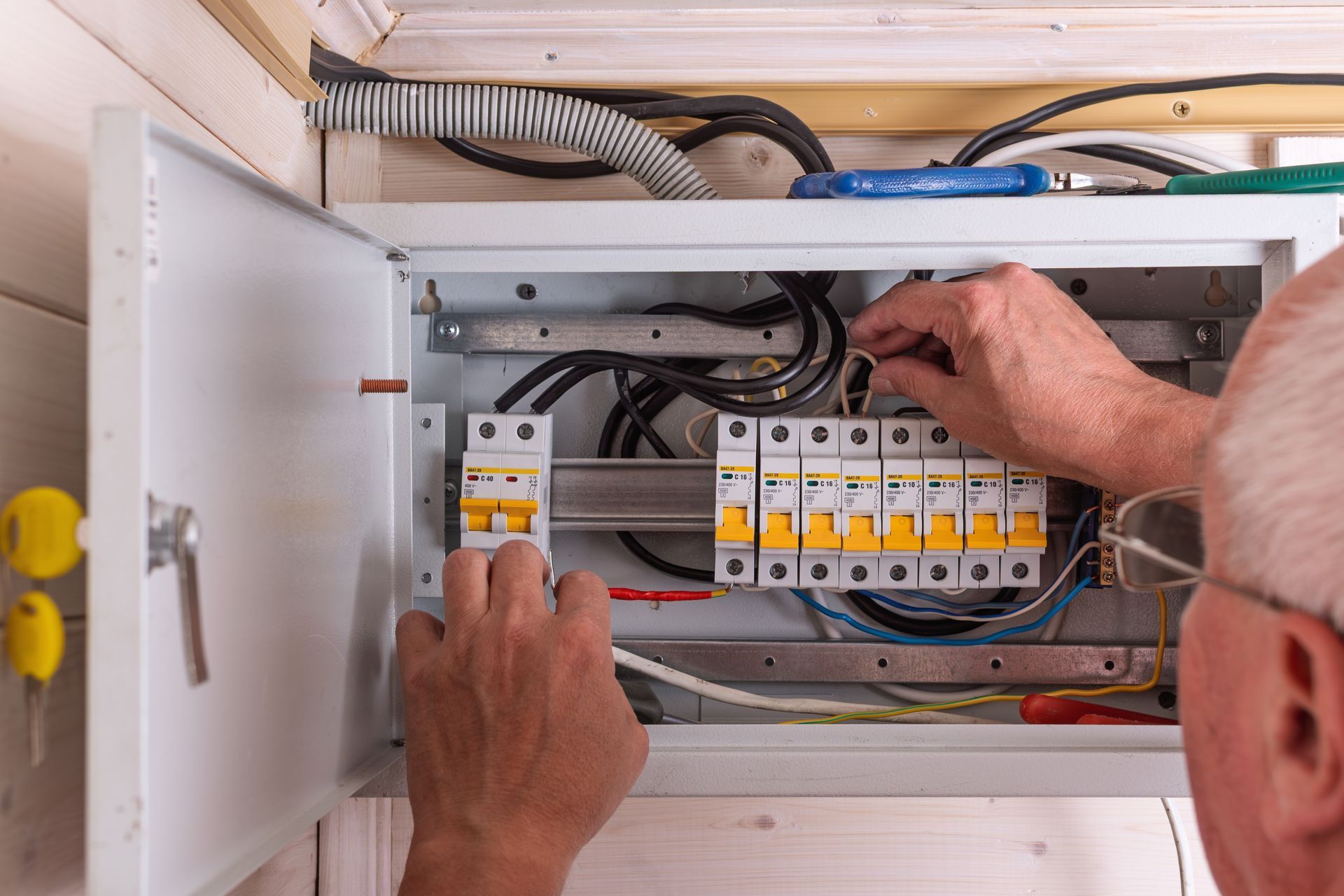 Hands wiring an electrical breaker panel in an open cabinet