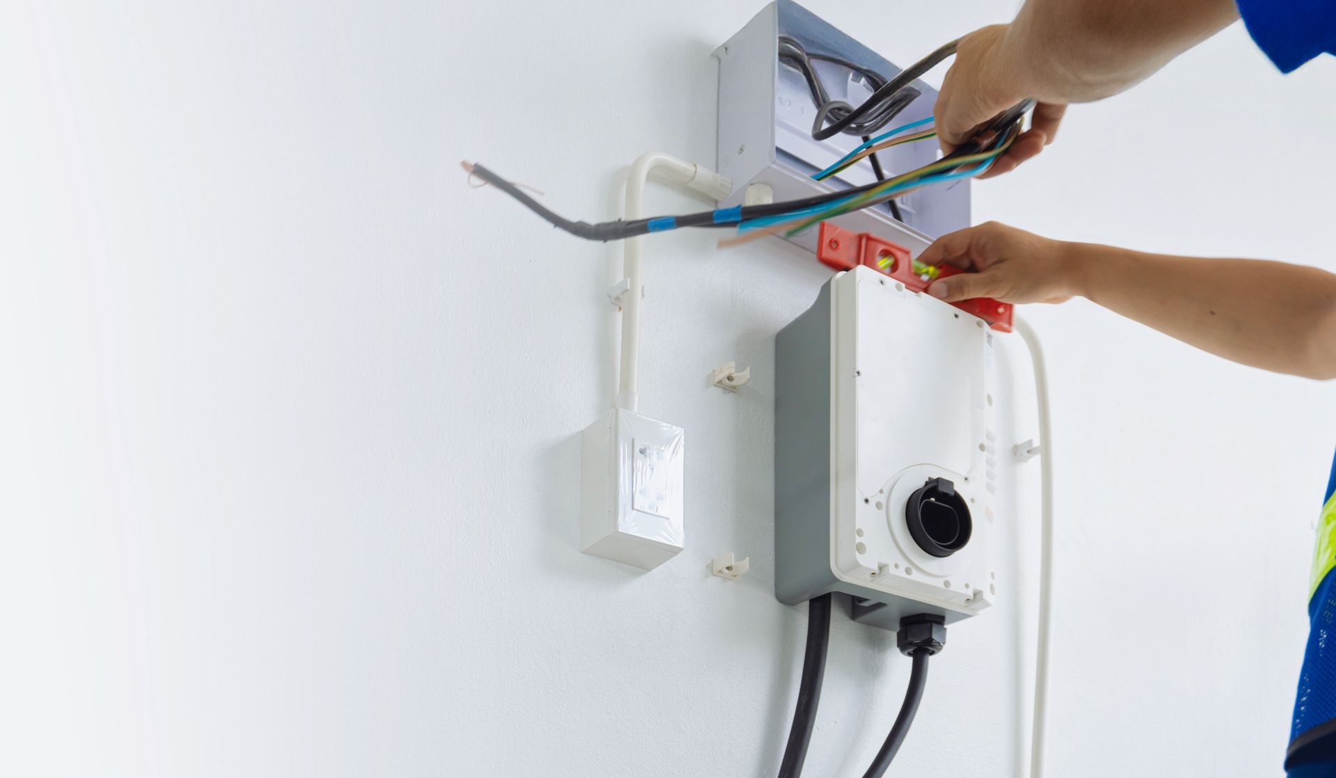 Hands wiring a wall-mounted white boiler with exposed colored cables during installation