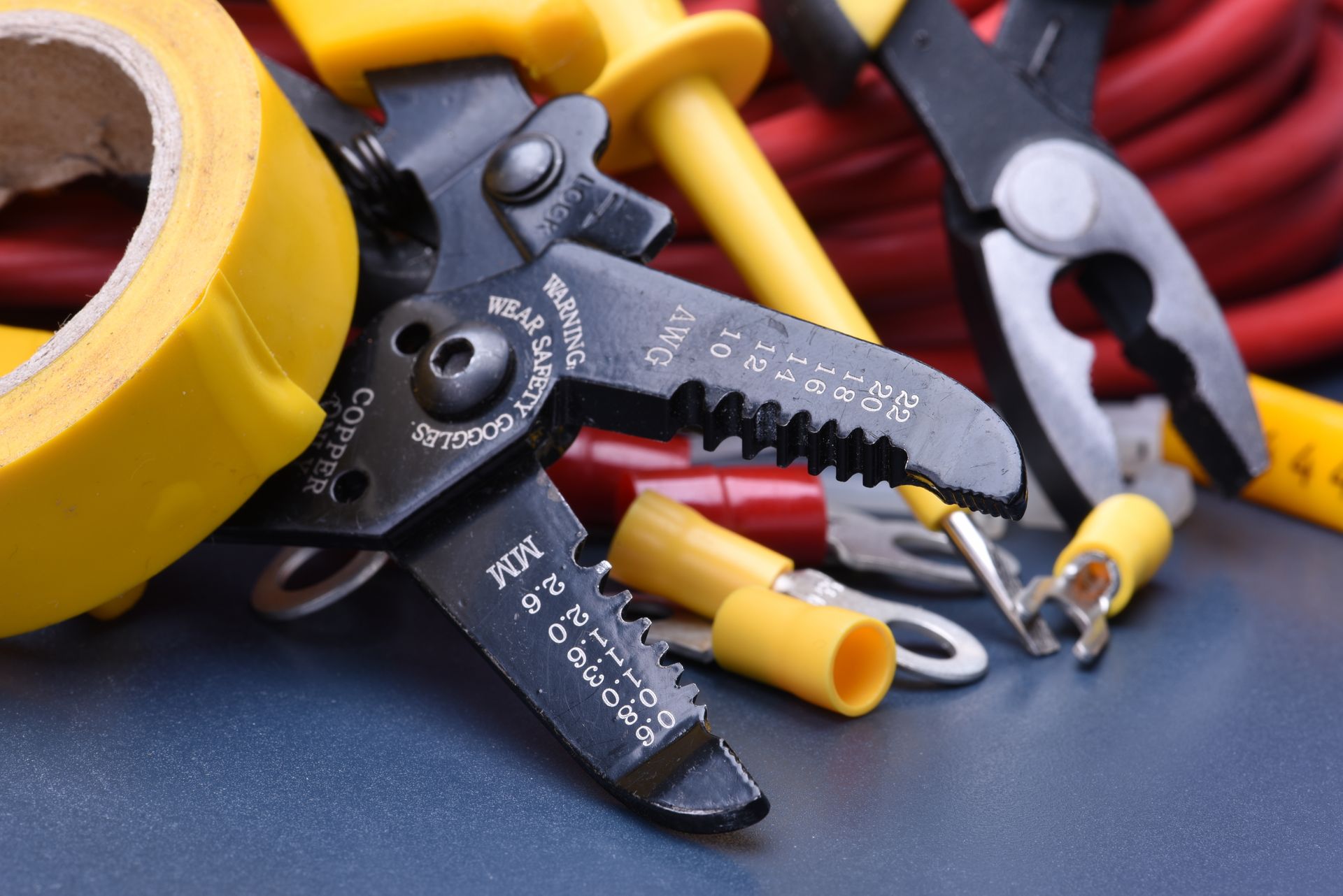Assorted electrical tools, wire strippers, cutters, and yellow tape on a dark surface