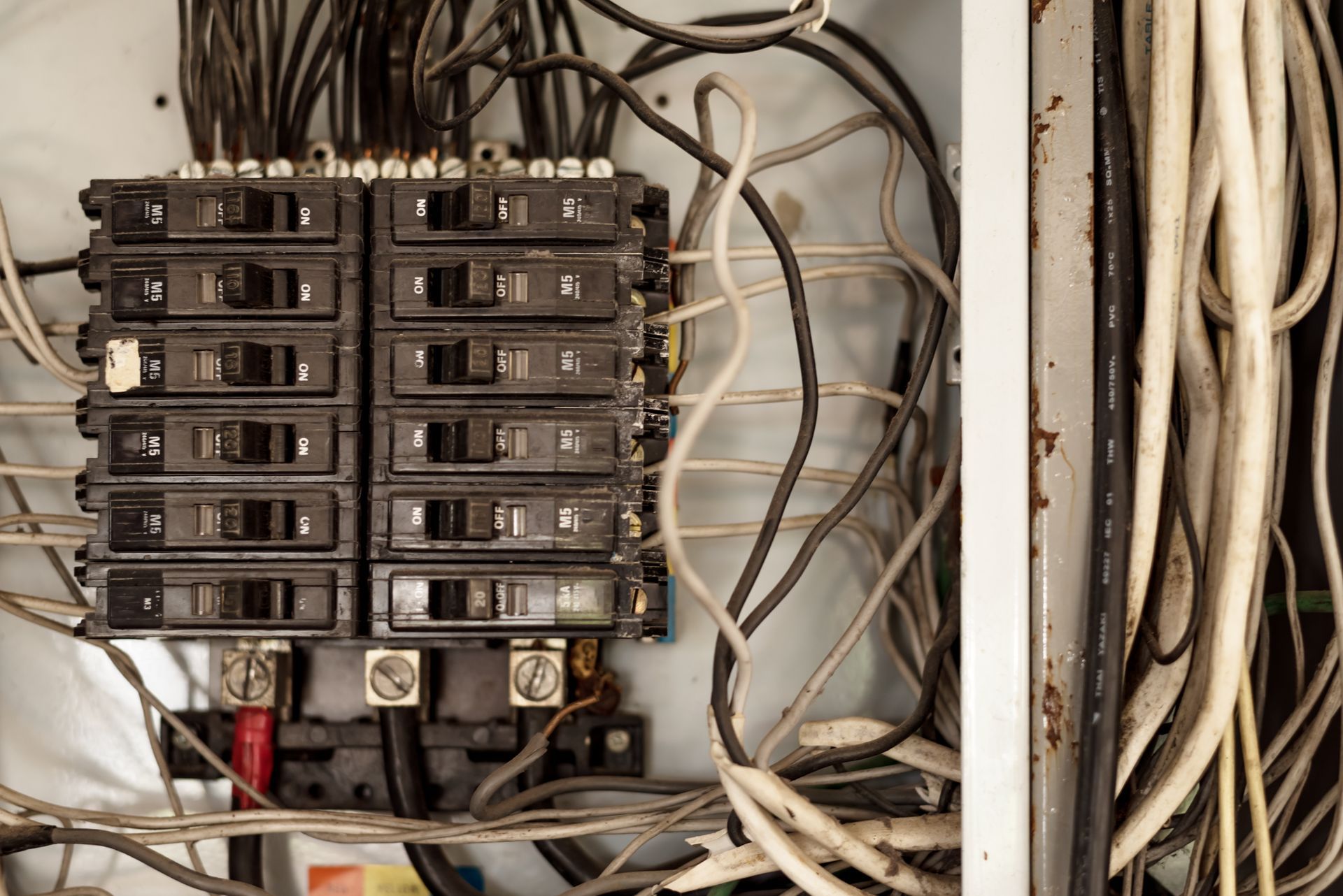 Electrical breaker panel with exposed wiring and multiple circuit breakers in a utility area