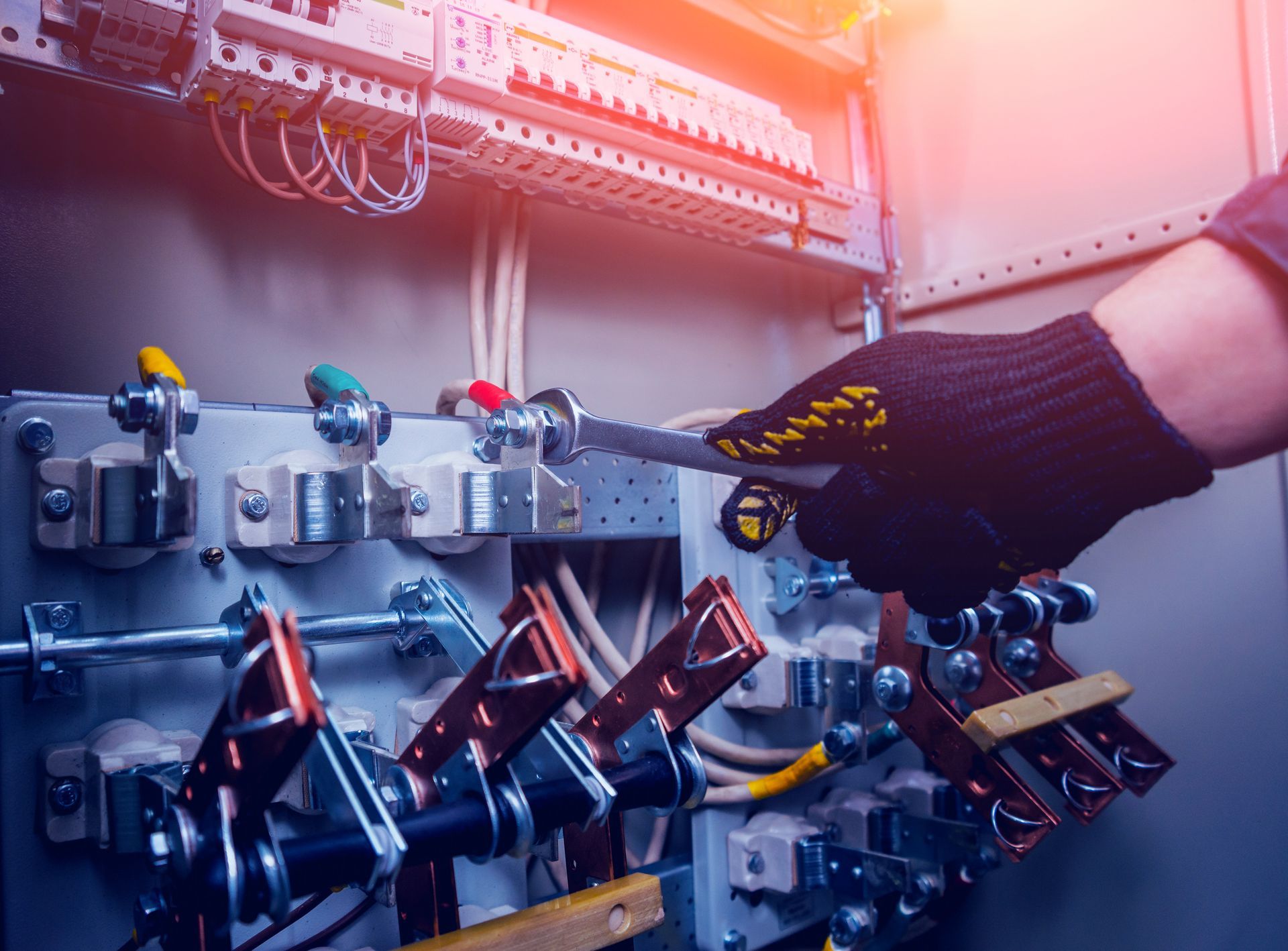 Gloved hand adjusting controls on an industrial machine with metal components and orange overhead light