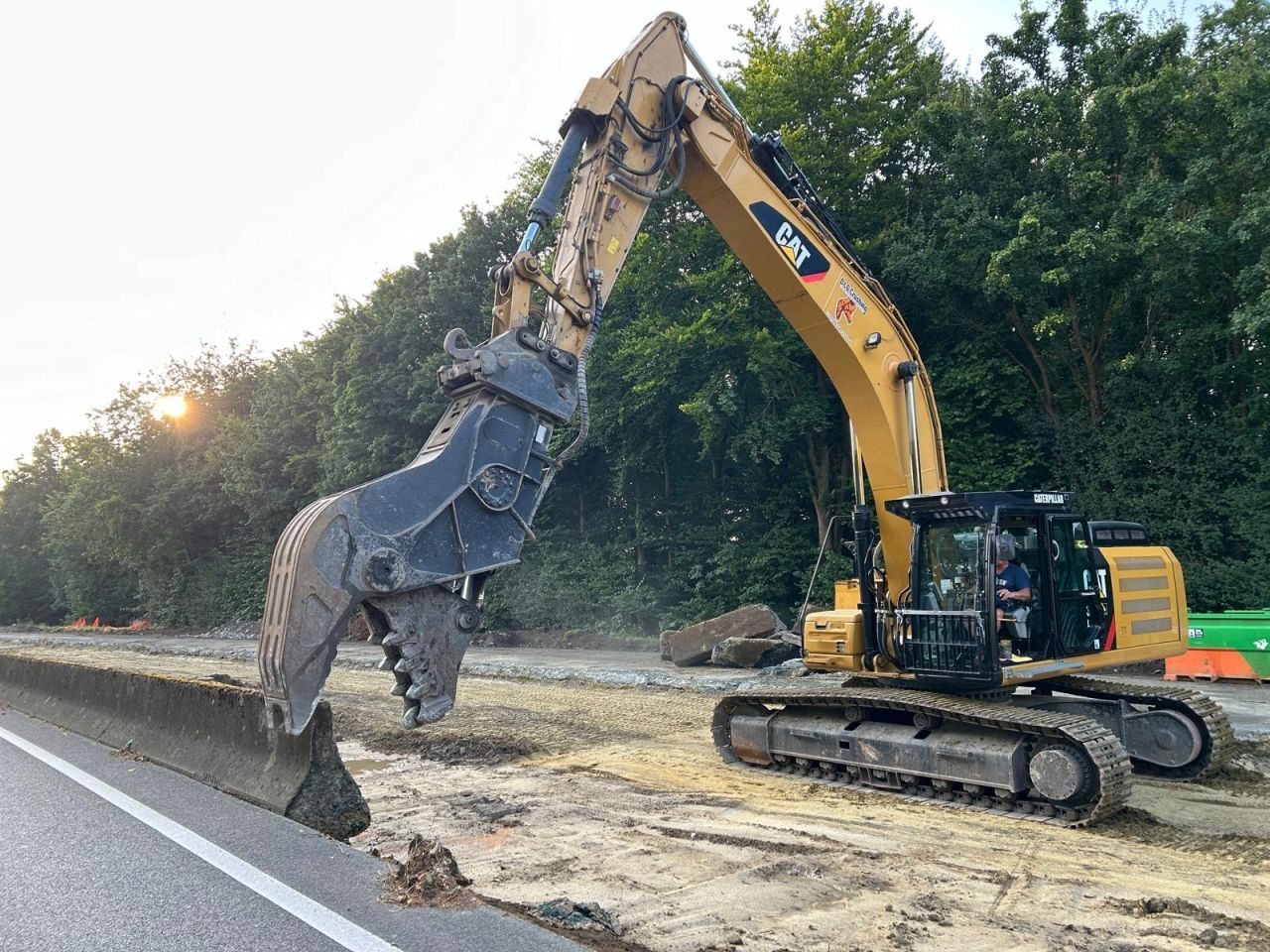 Gele graafmachine sloopt wegdek langs bomen