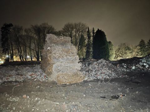 Nachtscène van een ruw stenen bouwwerk te midden van puin, met kale bomen als silhouetten op de achtergrond.