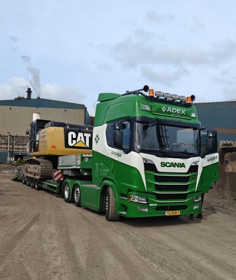 Groene Scania vrachtwagen met oplegger die een CAT graafmachine vervoert.