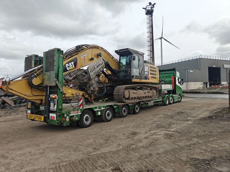 Groene vrachtwagen met een gele Caterpillar-machine op een industrieterrein.