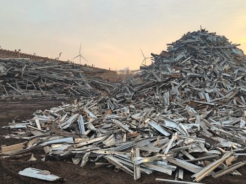 Grote hopen afvalhout en puin op een vuilstortplaats onder een bleke zonsondergang.