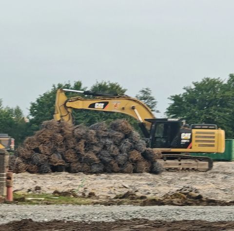 Gele graafmachine bovenop een grote stapel boomstammen op een bouwterrein.
