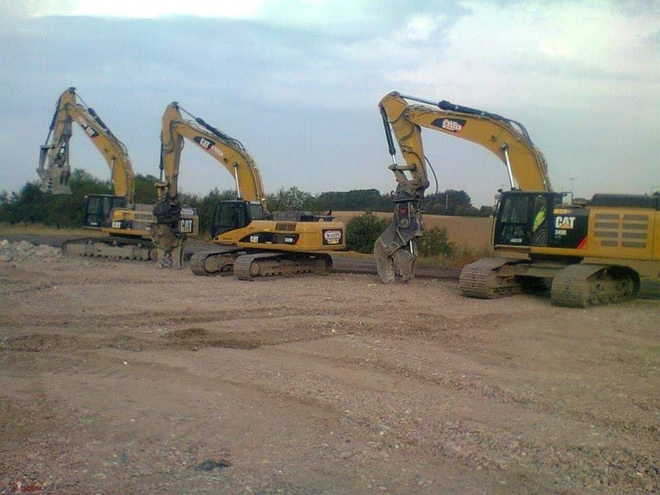 Drie gele graafmachines aan het werk op een onverhard bouwterrein onder een bewolkte hemel.