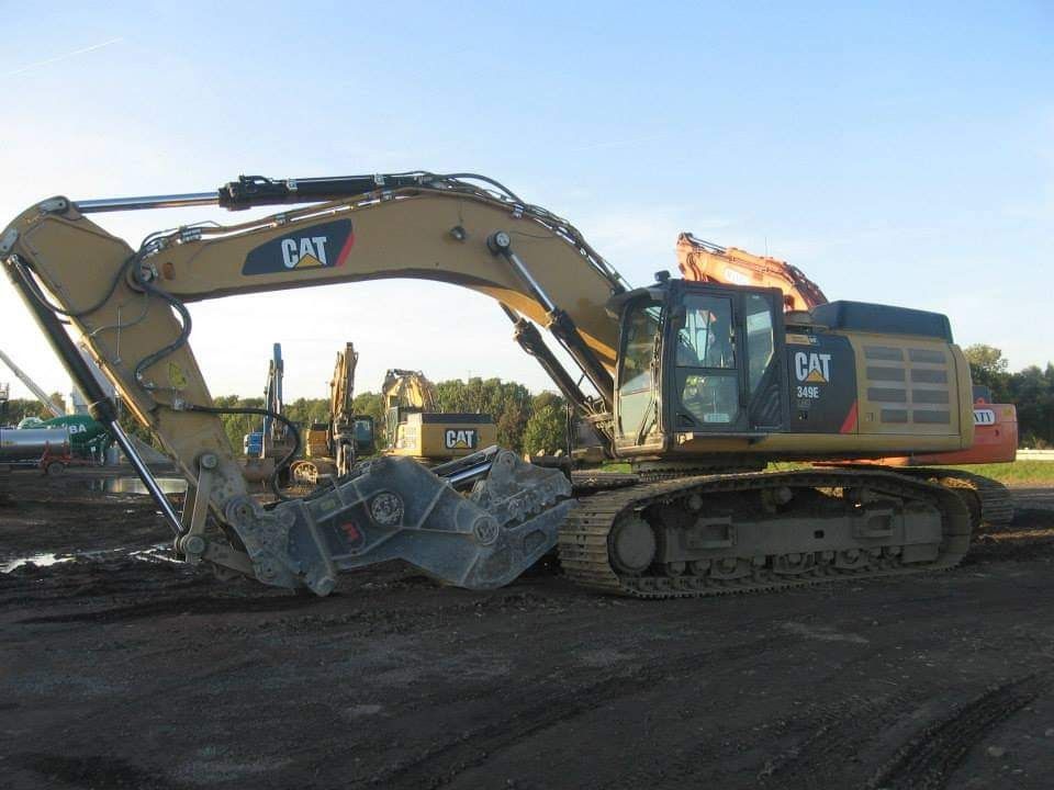 Een gele CAT-graafmachine op een bouwterrein houdt grote metalen brokken vast met de graafbak.