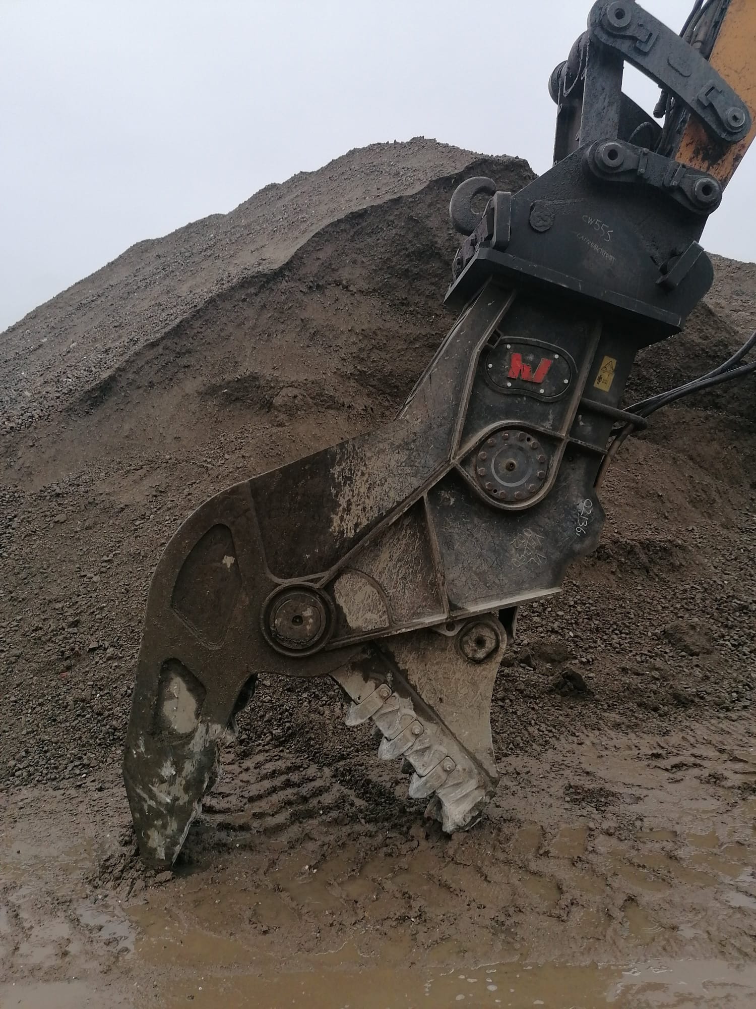 Een graafbak graaft in een grote hoop aarde en schept grond weg op een bouwterrein.
