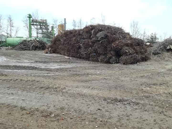 Grote hoop schroot op een industrieterrein met modderige grond en machines op de achtergrond.
