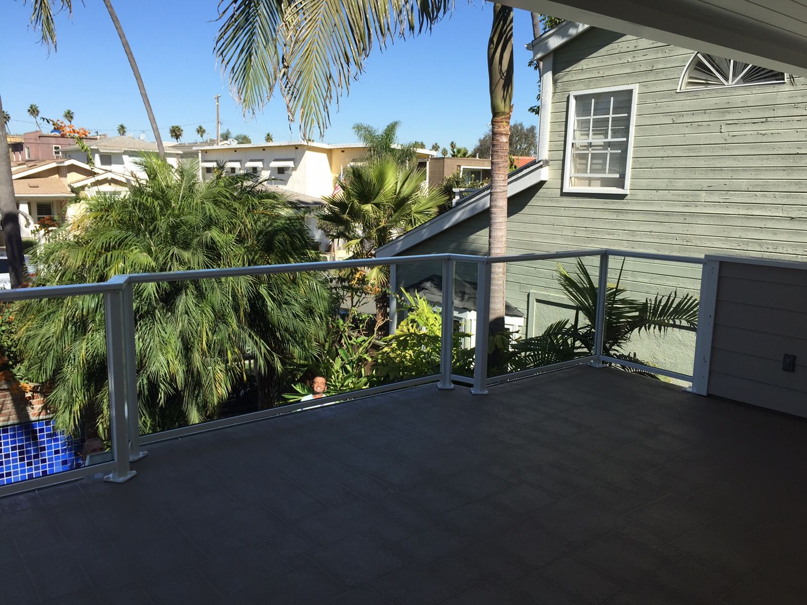Deck with glass railings overlooking lush greenery and houses on a sunny day.