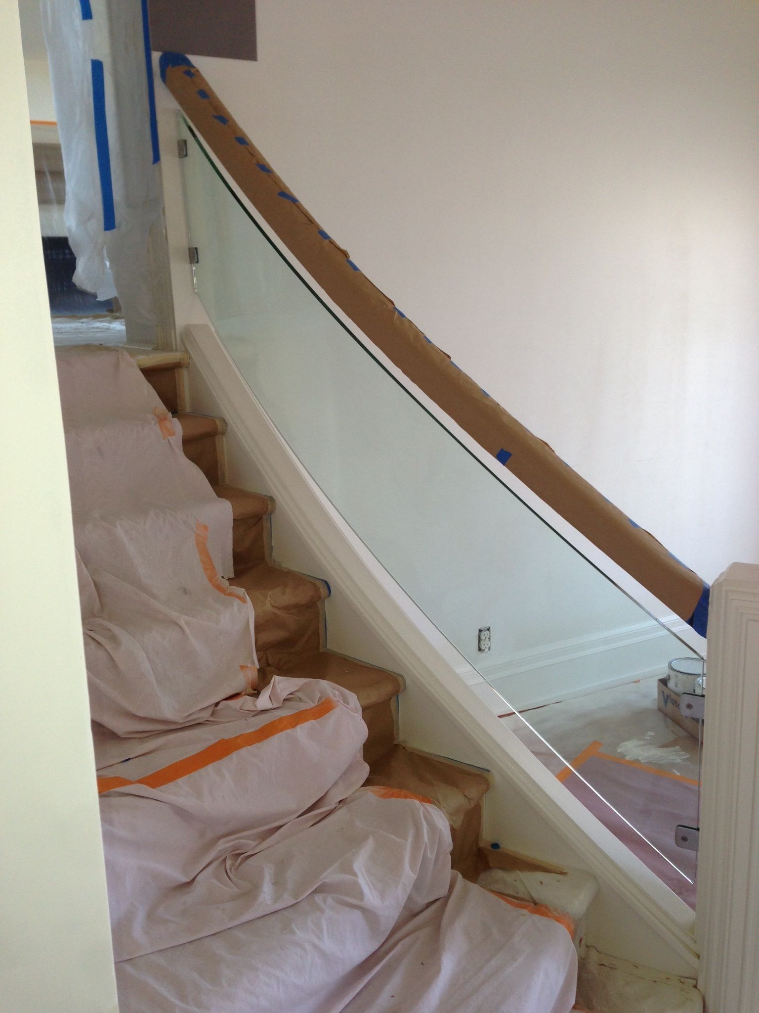 Staircase with curved glass railing and wooden handrail. Steps covered in protective material.
